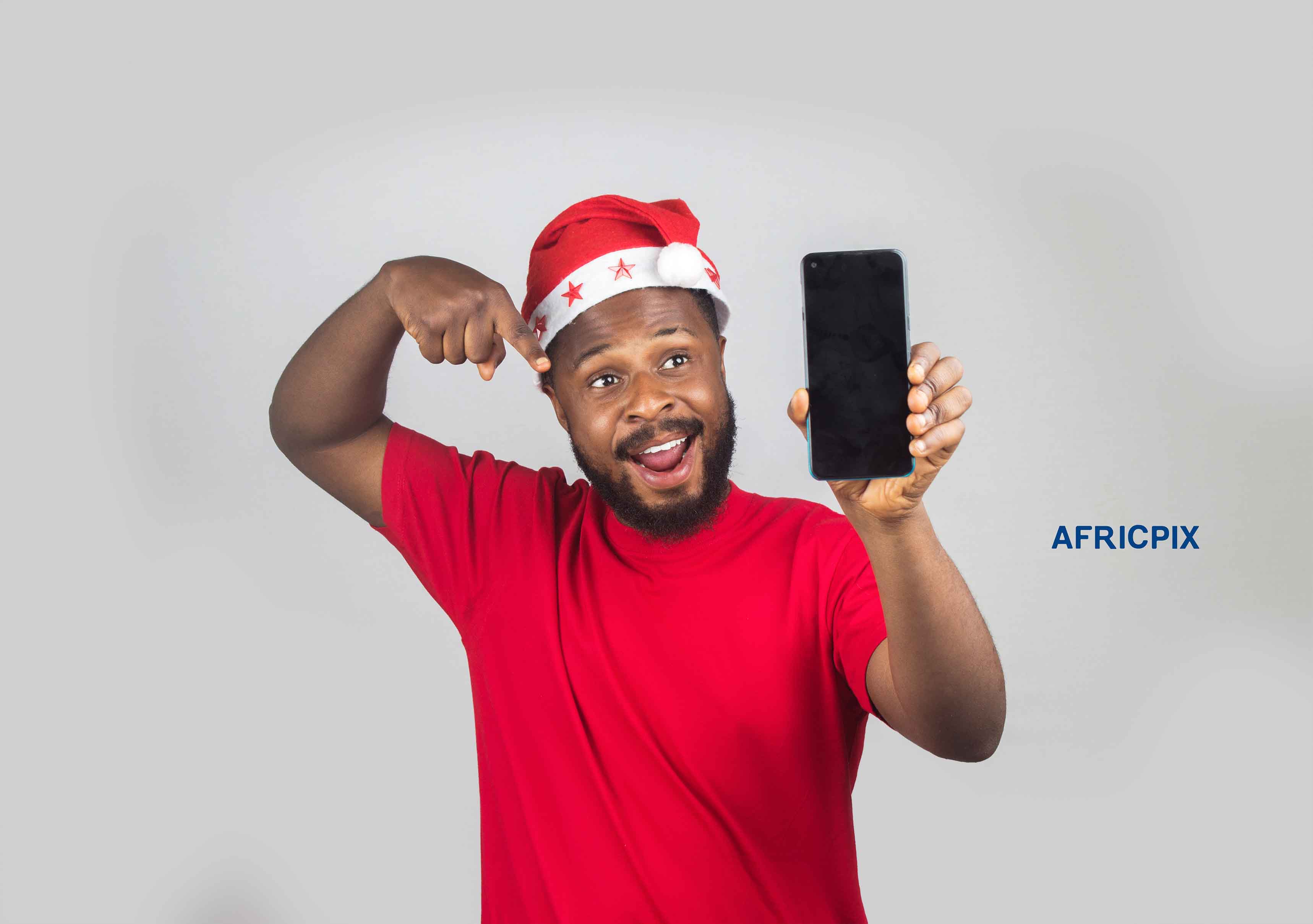 An African Nigerian man wearing a Christmas cap, holding a phone in one hand and pointing at it with the other hand 4.